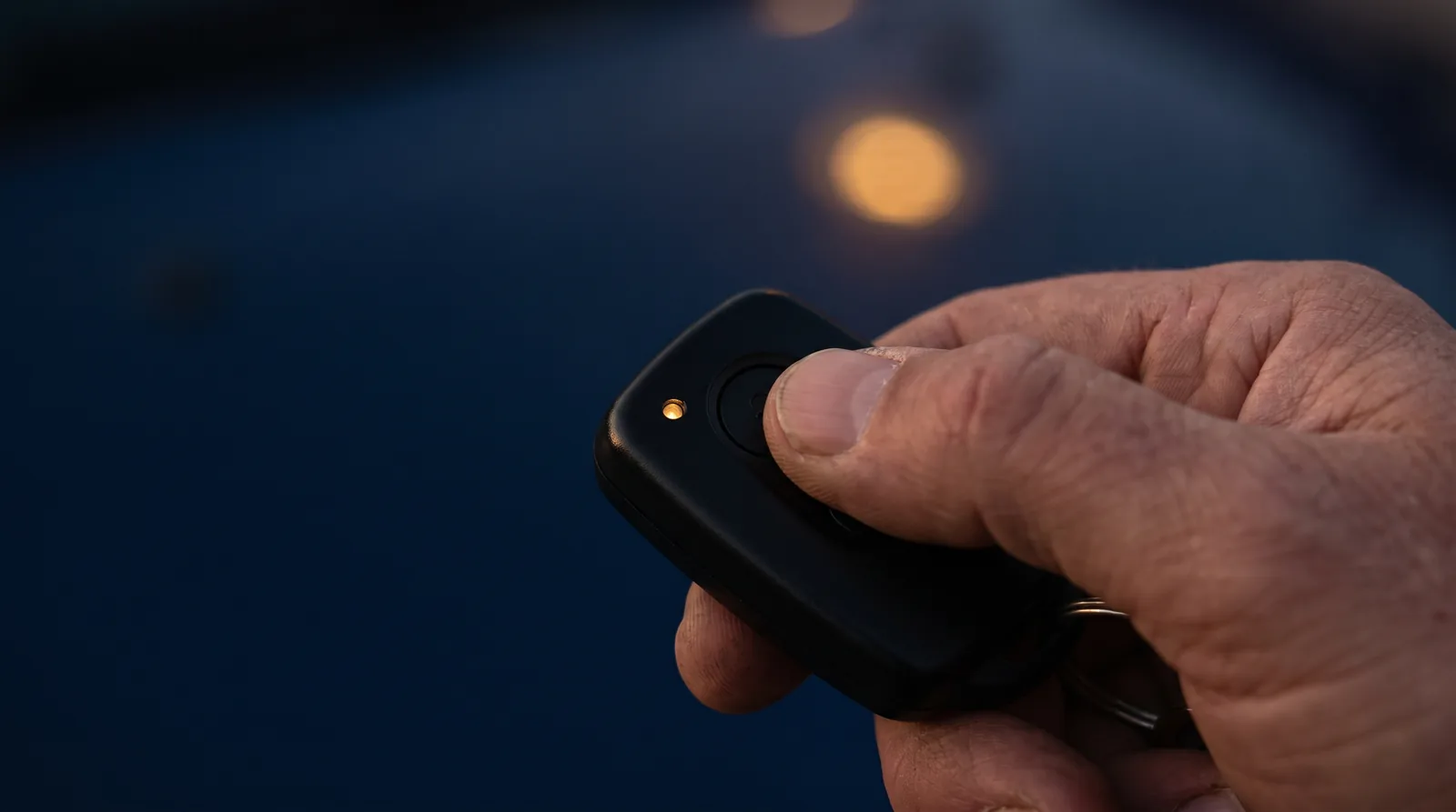 A hand pressing a button on a black car key fob